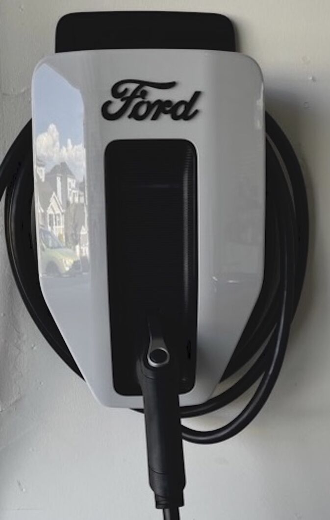 A Ford-branded electric vehicle charging station is mounted on a wall with its charging cable neatly coiled around it.