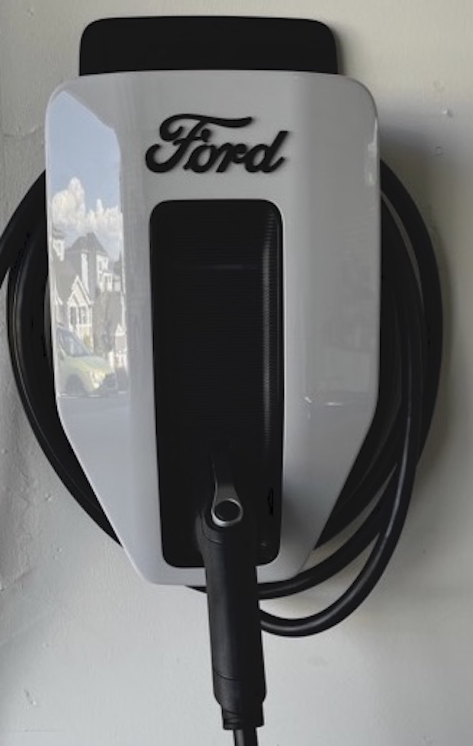 A Ford-branded electric vehicle charging station is mounted on a wall with its charging cable neatly coiled around it.