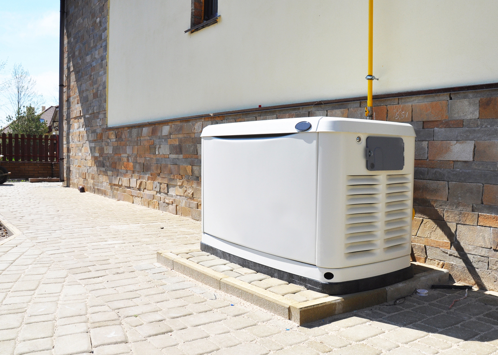 A white standby generator installation is completed on a concrete pad next to a house with a stone and stucco exterior.